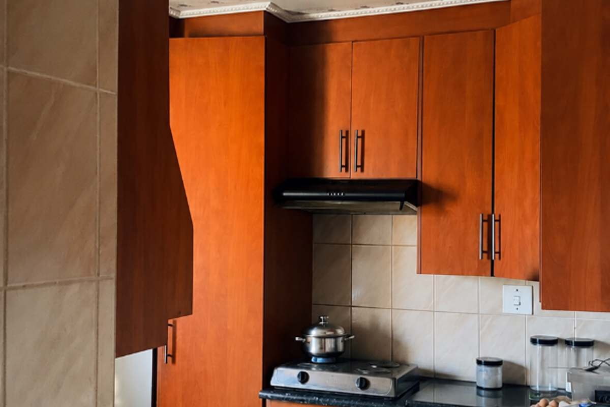 A functional kitchen featuring warm-toned wooden cabinetry, granite countertops, a built-in oven with gas hob, and a tiled backsplash.