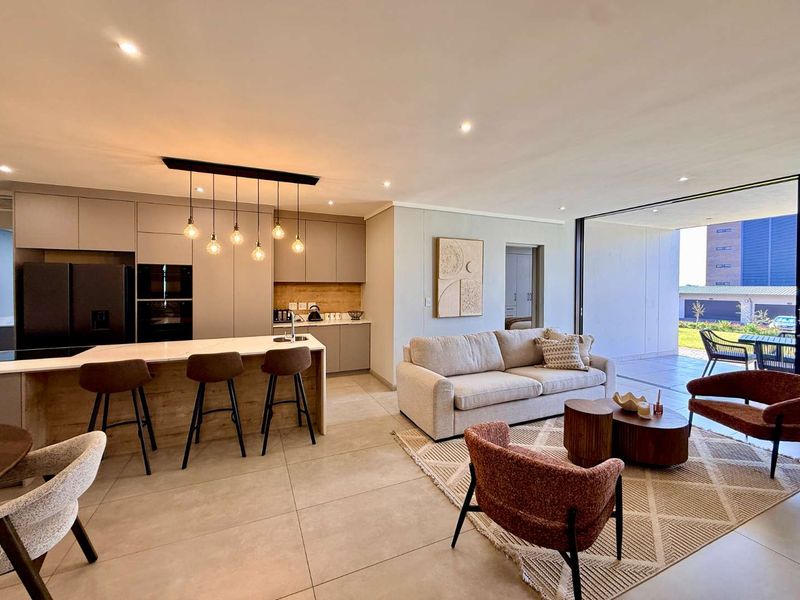 Modern open-plan living area featuring a sleek kitchen with stone island, recessed lighting, and seamless flow to a covered patio through large sliding doors.
