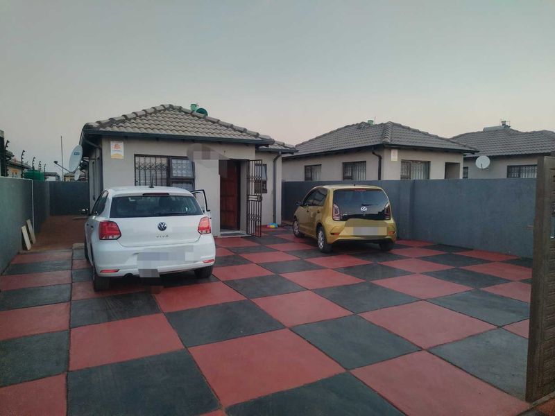 Front view of a residential house featuring a paved driveway with a checkered pattern and a secure perimeter wall.