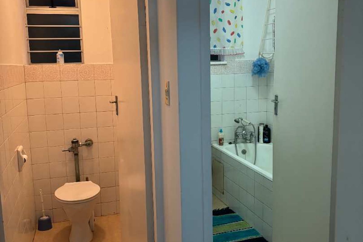 A view of a separate toilet and bathroom area featuring basic sanitary ware, tiled walls, and overhead lighting.