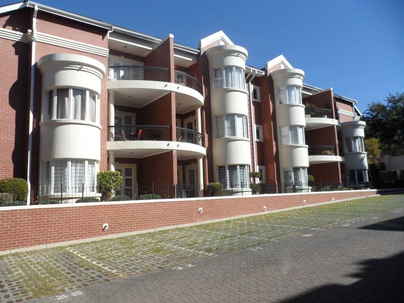 Exterior view of a multi-story apartment complex featuring red brick facade, curved balconies with iron railings, and dedicated paved parking spaces.