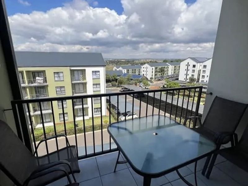 A covered balcony featuring tiled flooring and a metal balustrade, offering an elevated view of the surrounding apartment complex.