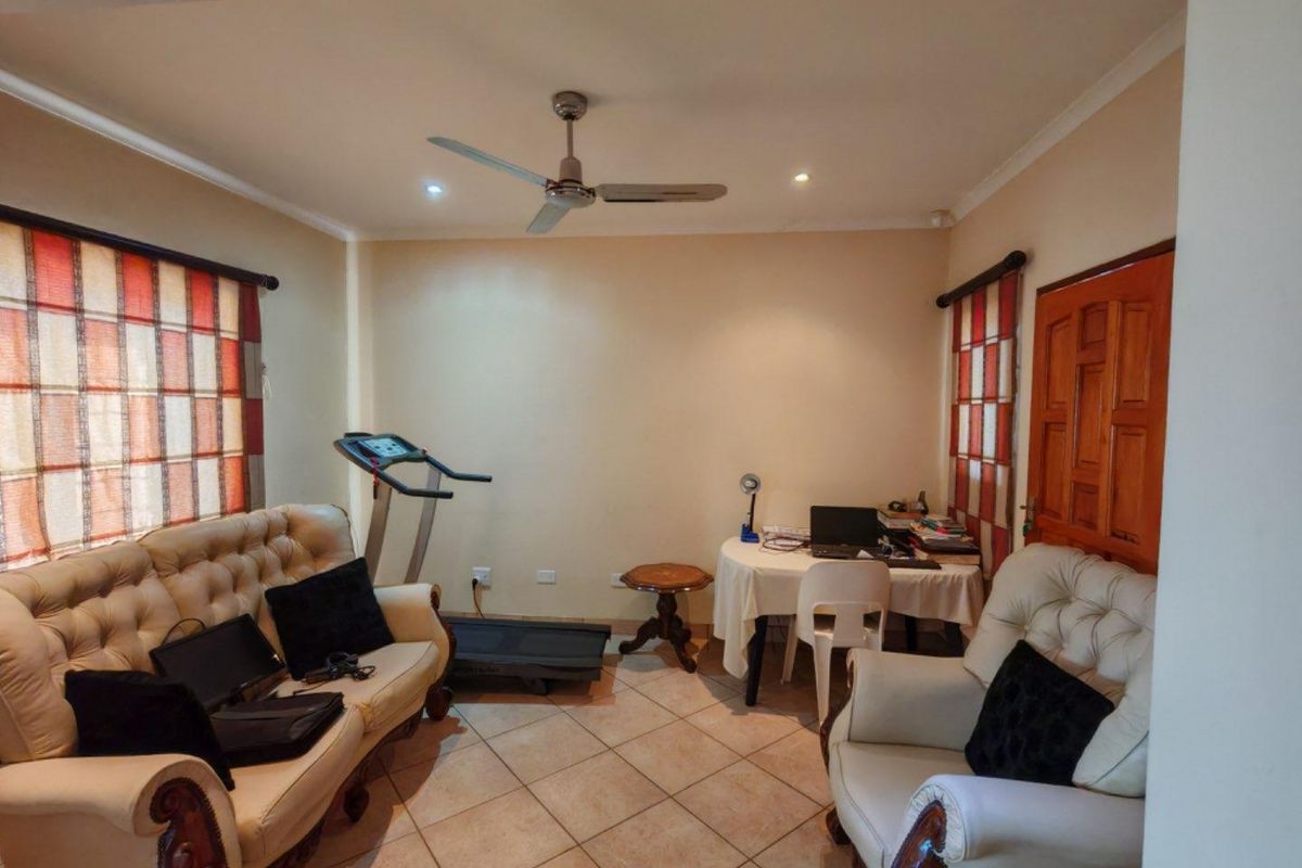 A multi-purpose living area featuring tiled flooring, a ceiling fan, and recessed lighting, currently utilized as a combined lounge and home office space.