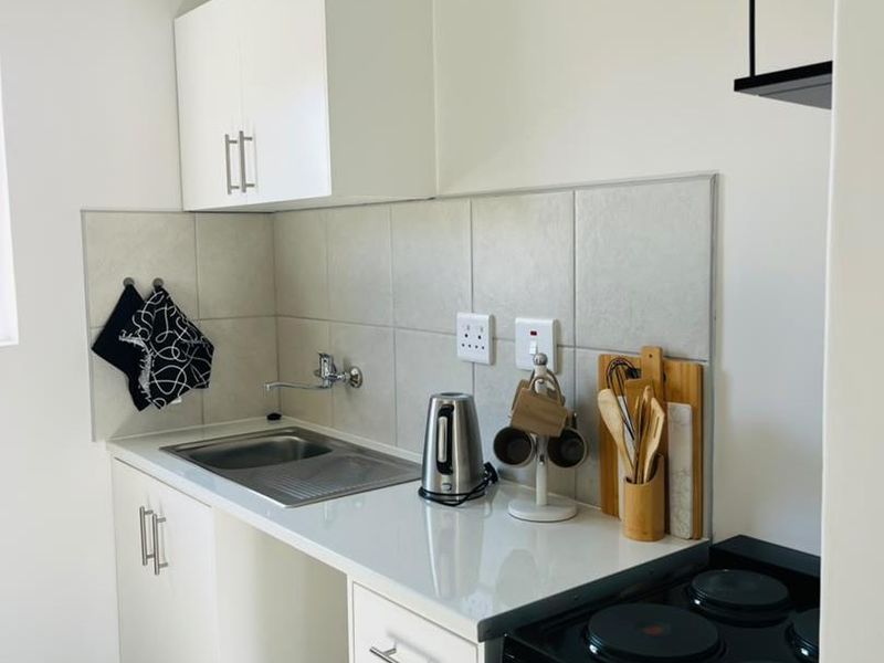 A compact, well-maintained kitchen featuring white cabinetry, a stainless steel sink, tiled backsplash, and a freestanding electric stove.