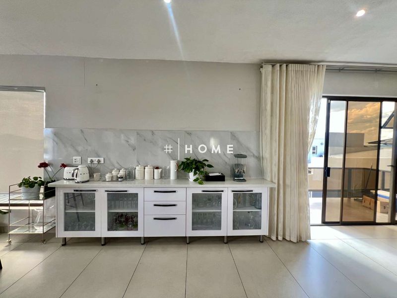 A modern kitchen area featuring white cabinetry, stone countertops, and a marble-look splashback, with direct access to an outdoor patio through sliding glass doors.