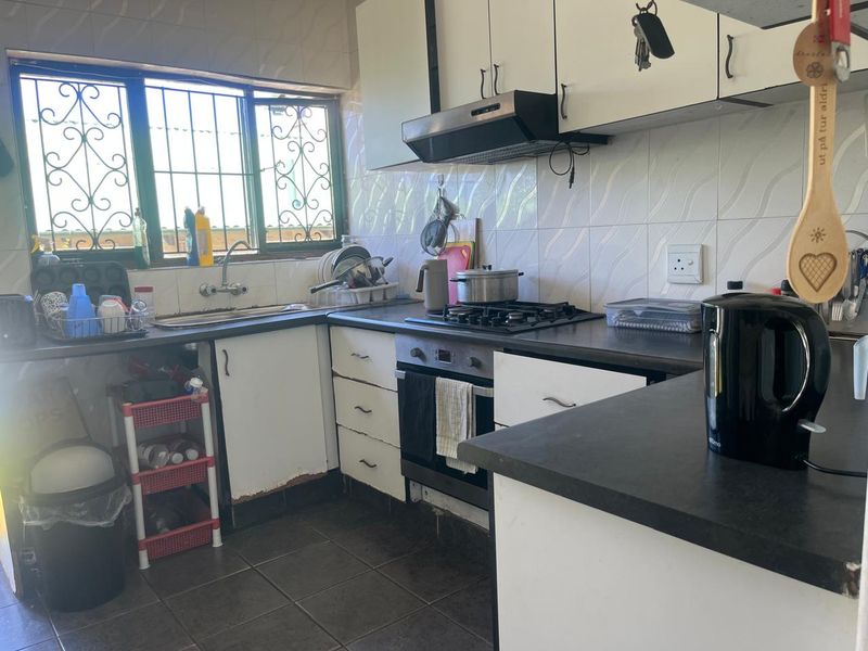 A functional kitchen featuring built-in cabinetry, a gas hob, oven, and extractor fan, with tiled backsplash and security bars on the window.
