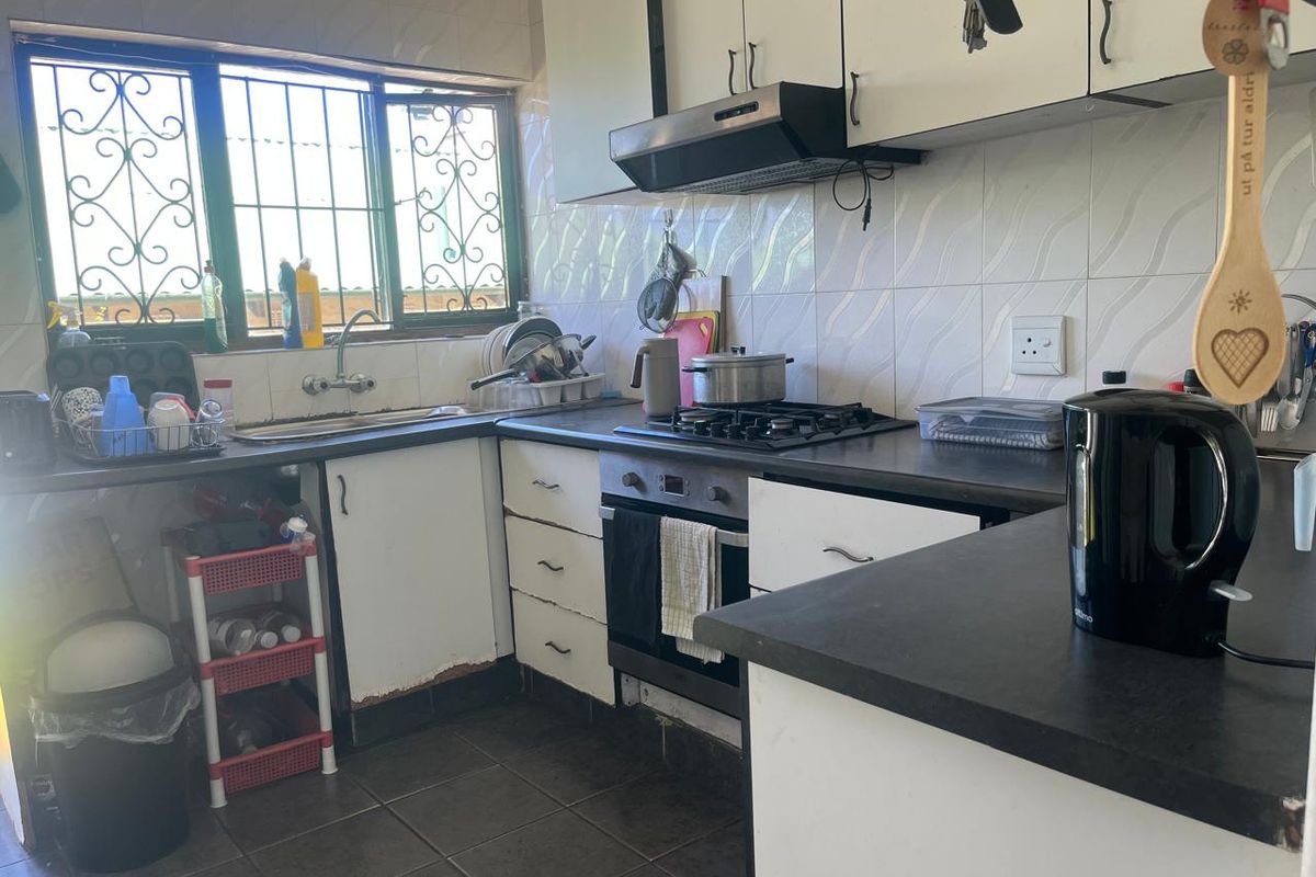 A functional kitchen featuring built-in cabinetry, a gas hob, oven, and extractor fan, with tiled backsplash and security bars on the window.