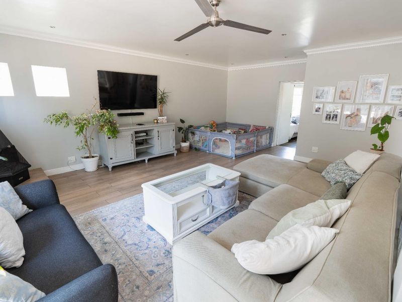 Spacious living room featuring laminate flooring, coved cornicing, a ceiling fan, and a freestanding fireplace, creating a comfortable and inviting family space.