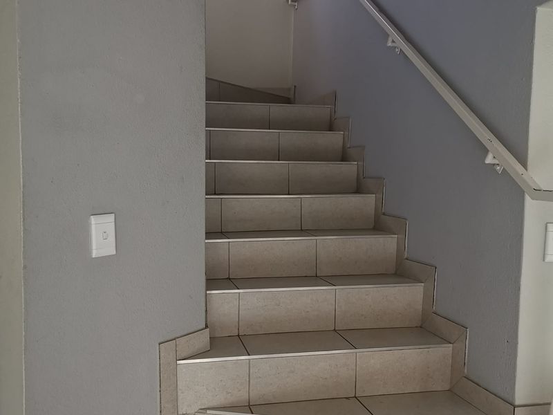 A clean, tiled staircase featuring a white metal handrail and neutral grey wall finishes, providing access between levels.