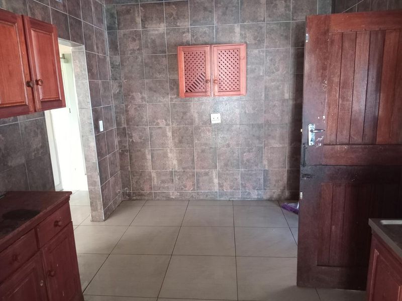 A dated kitchen area featuring full-height wall tiling, tiled flooring, and traditional wooden cabinetry, presenting an opportunity for modernization.