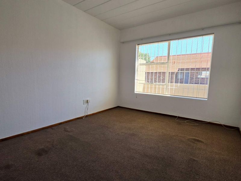 A vacant bedroom featuring carpeted flooring, a large window with security bars, and neutral wall finishes, ready for personalization.