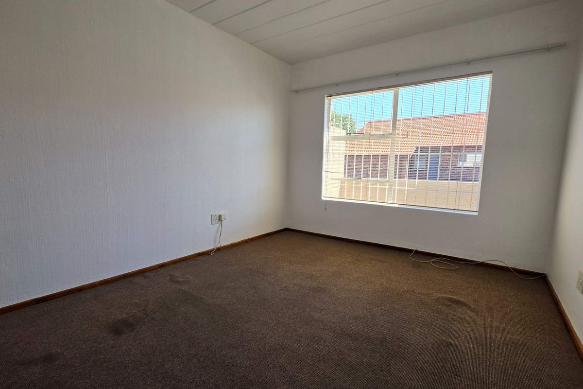 A vacant bedroom featuring carpeted flooring, a large window with security bars, and neutral wall finishes, ready for personalization.