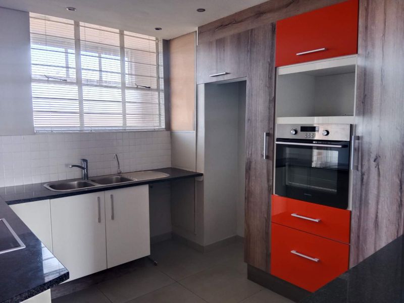 A modern kitchen featuring high-contrast orange and wood-grain cabinetry, granite countertops, a built-in oven, and a double sink with a tiled backsplash.