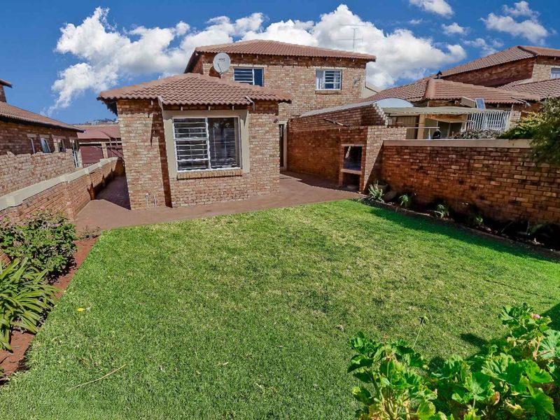 Rear view of the townhouse featuring a private garden, paved patio area, and a built-in brick braai facility.