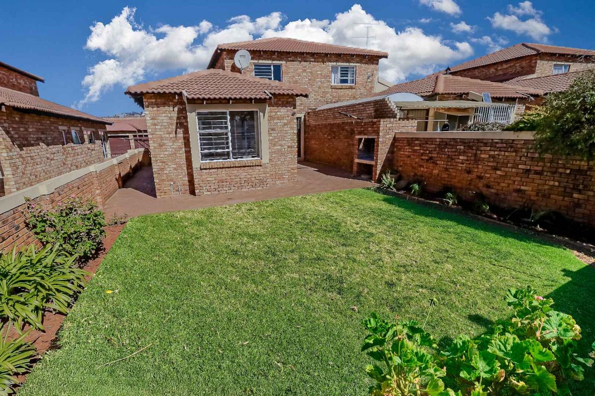 Rear view of the townhouse featuring a private garden, paved patio area, and a built-in brick braai facility.