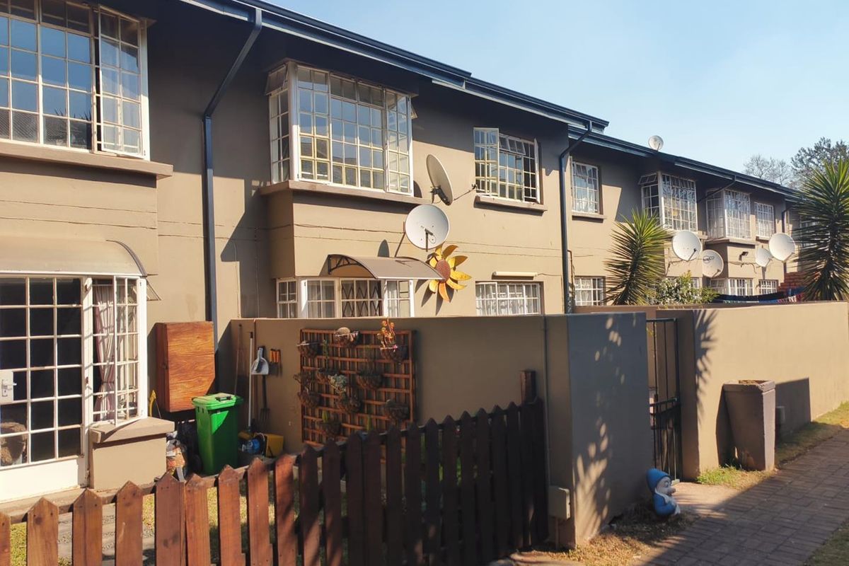 Rear exterior view of a multi-story apartment block featuring steel-framed windows, a private courtyard area with boundary wall, and timber fencing.