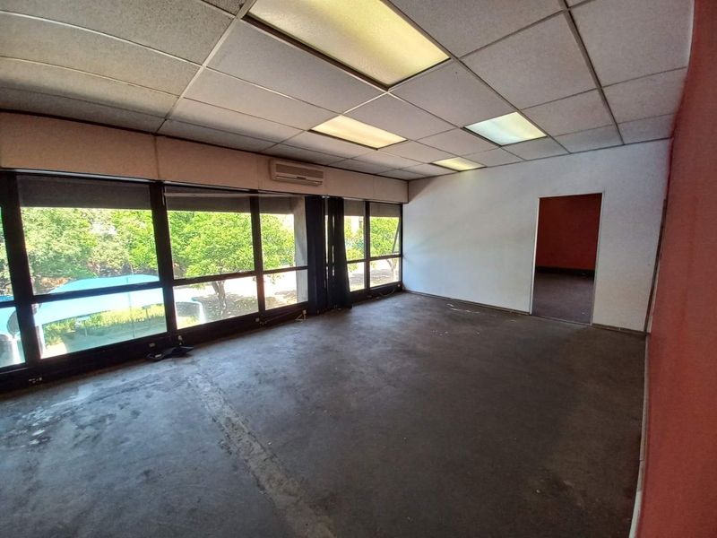 An empty office space featuring large windows, a drop ceiling with integrated lighting, and a wall-mounted air conditioning unit.