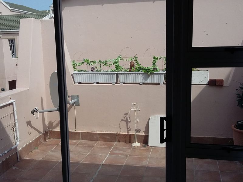A private outdoor patio area featuring tiled flooring and enclosed by parapet walls, accessible via a sliding glass door.