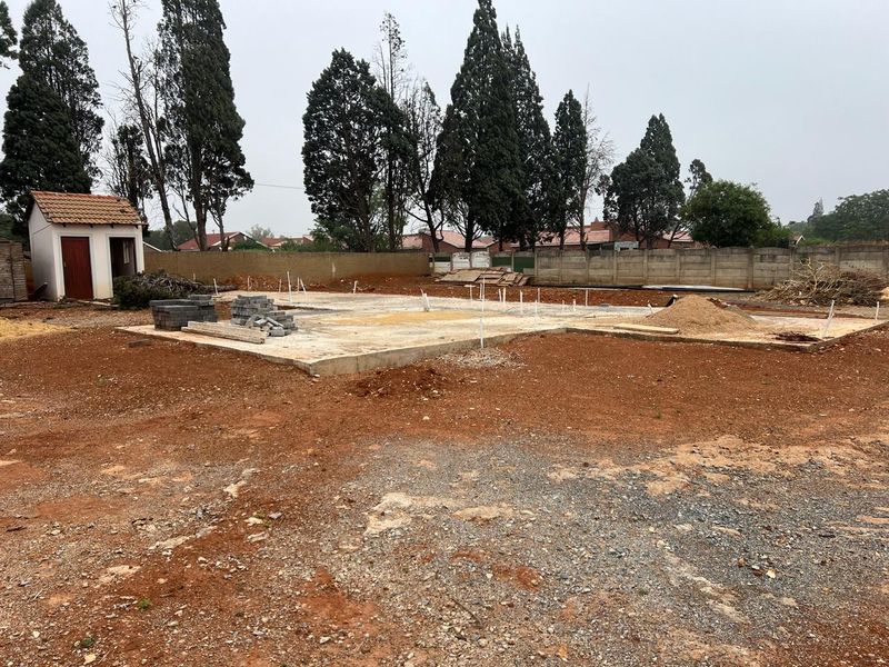 Vacant residential land featuring a concrete slab foundation, perimeter boundary wall, and a small outbuilding, ready for further development.