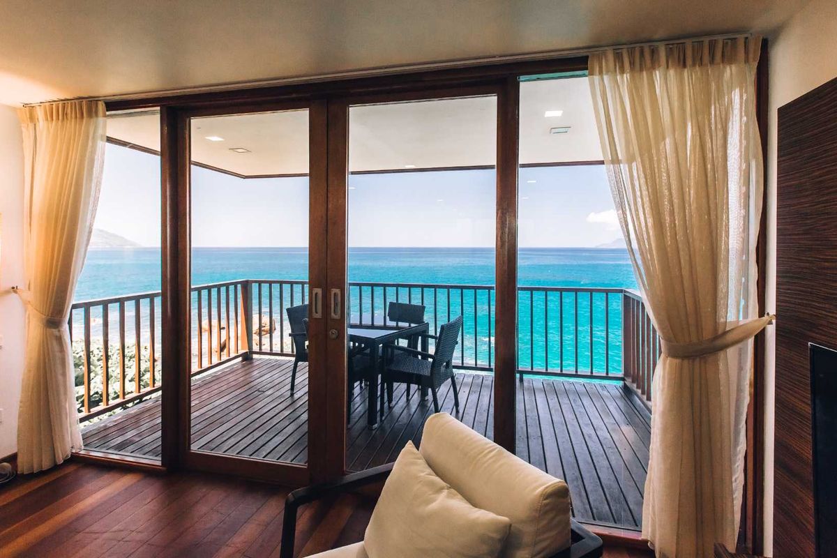 A bright living area featuring large timber-framed sliding glass doors that open onto a private balcony with expansive ocean views.