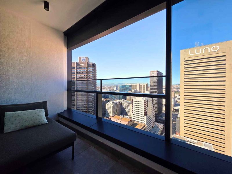 A modern enclosed balcony featuring floor-to-ceiling windows with expansive urban city views and sleek tiled flooring.