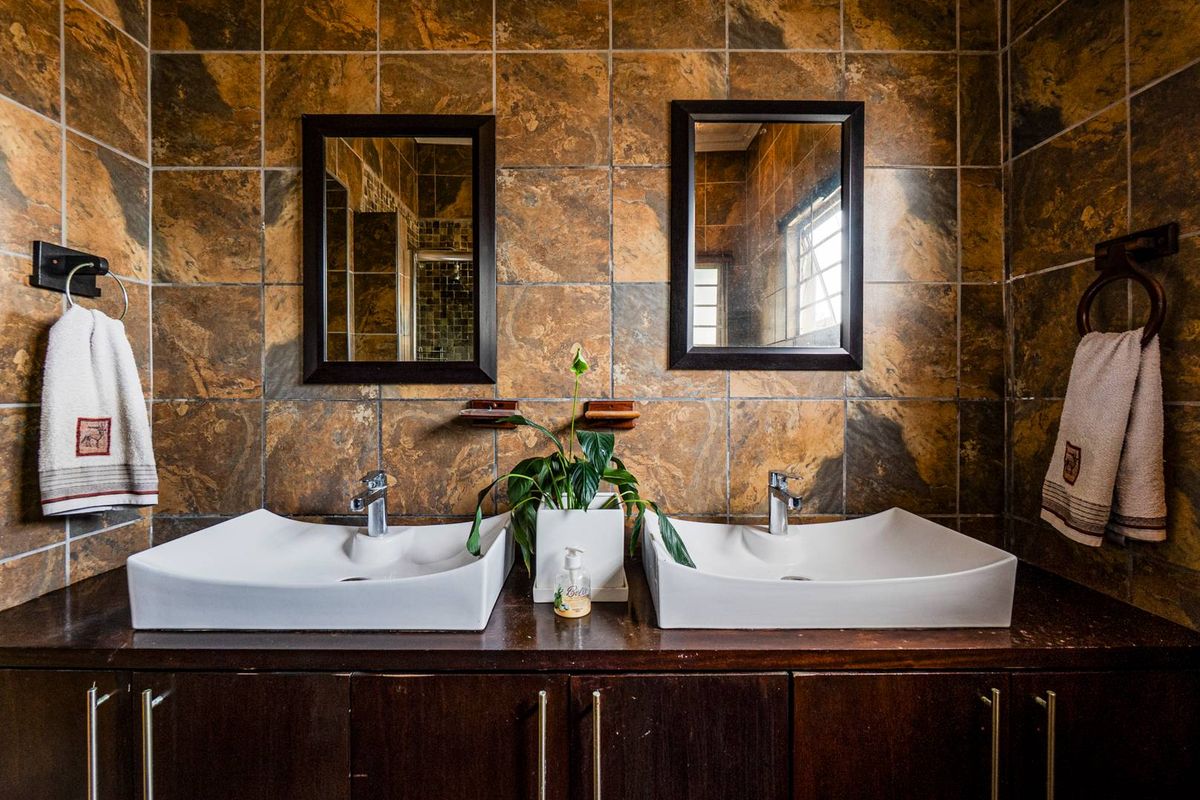 A bathroom vanity featuring dual vessel sinks, dark wood cabinetry, and full-height stone-look wall tiling with two framed mirrors.