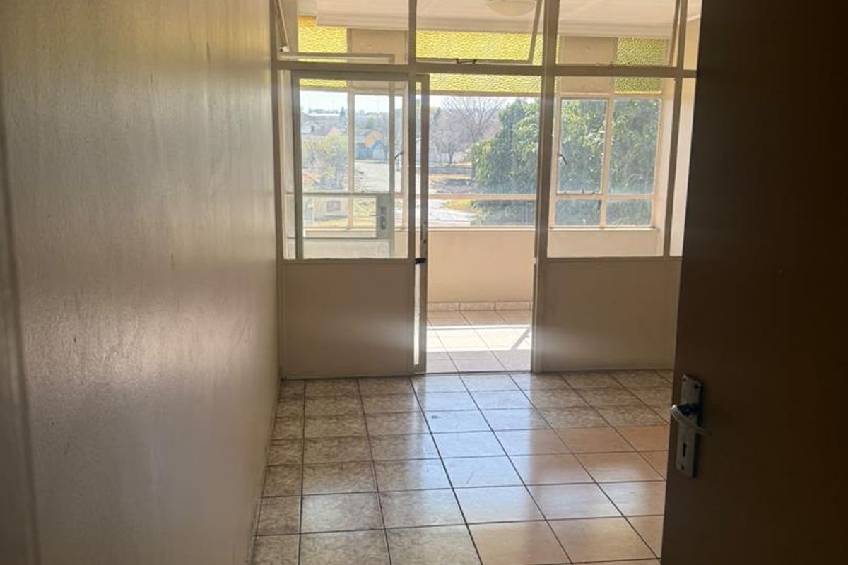 An empty living area featuring tiled flooring and large glass panels leading to an outdoor balcony, offering natural light and a view.