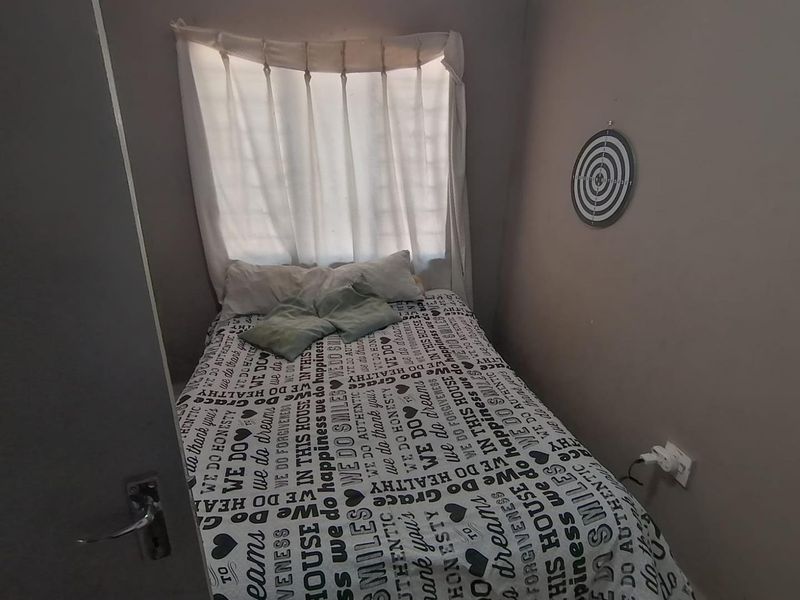 A compact bedroom featuring neutral wall tones and a window with fitted curtaining, providing a functional sleeping space.