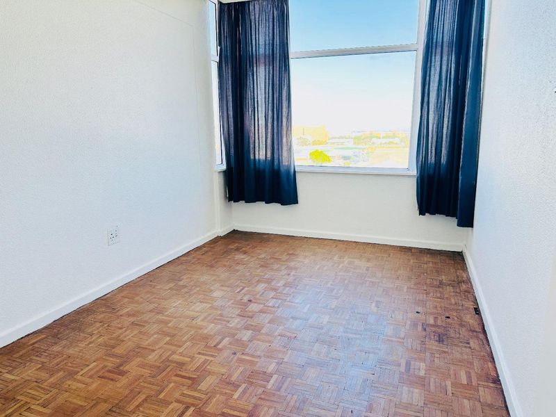 An empty bedroom featuring original parquet flooring and a large window with natural light, offering a blank canvas for renovation.