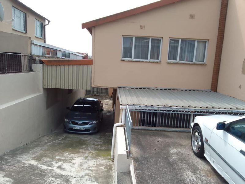Rear exterior view of the property featuring a concrete driveway, covered parking area, and metal security railings.