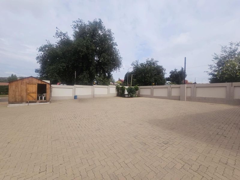 A spacious paved outdoor area featuring a perimeter boundary wall with electric fencing and a small wooden storage shed.