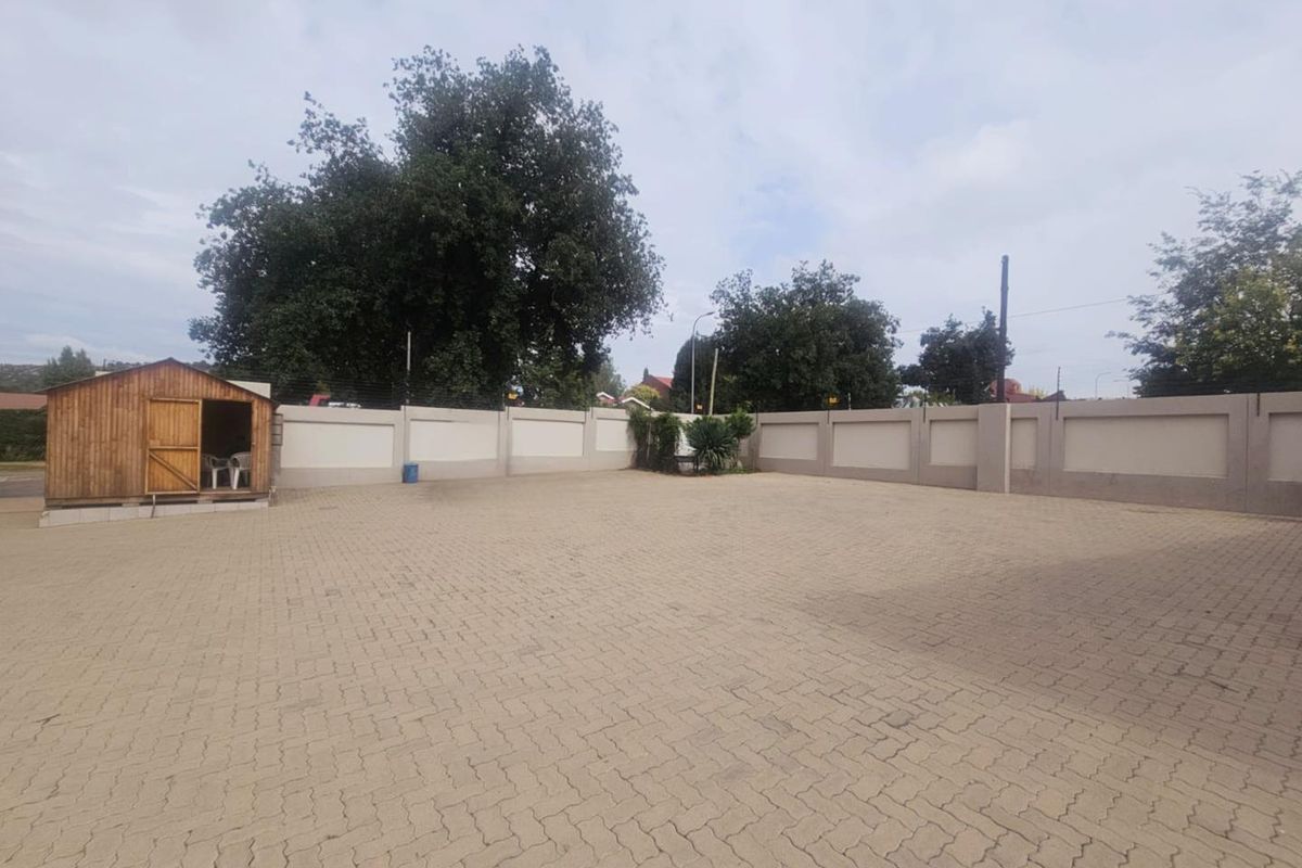 A spacious paved outdoor area featuring a perimeter boundary wall with electric fencing and a small wooden storage shed.