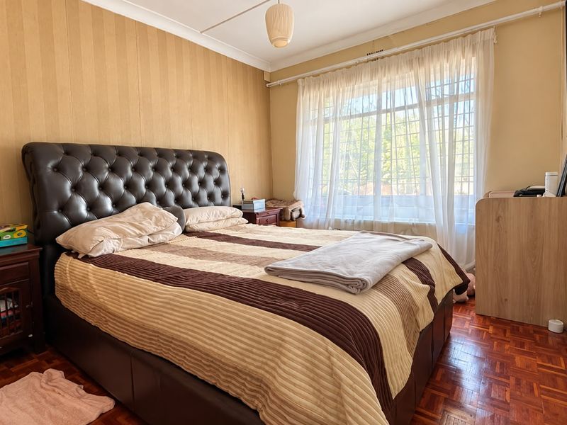 A bedroom featuring parquet flooring, coved ceilings, and window security bars, offering a functional space with potential for cosmetic updates.