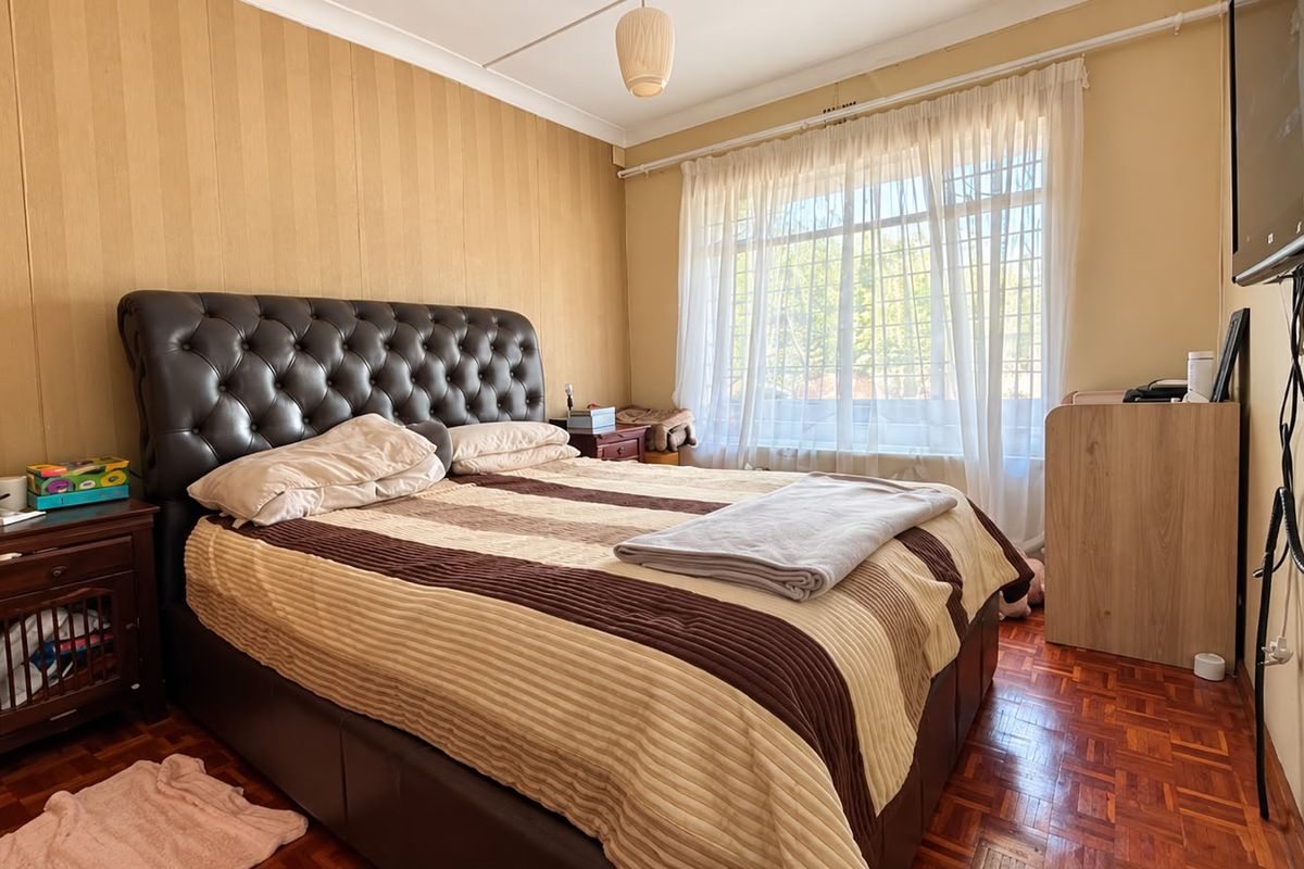 A bedroom featuring parquet flooring, coved ceilings, and window security bars, offering a functional space with potential for cosmetic updates.