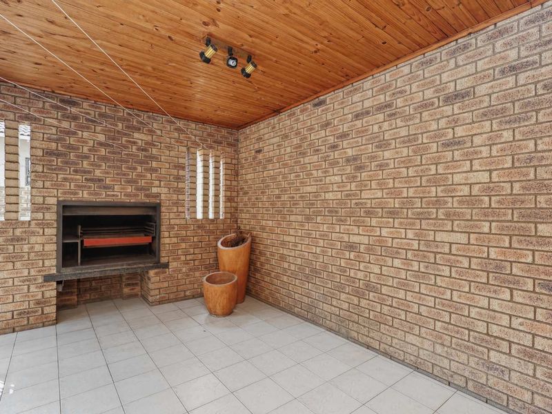 Covered patio area featuring exposed brick walls, a built-in braai, and a timber ceiling, providing a functional outdoor entertainment space.