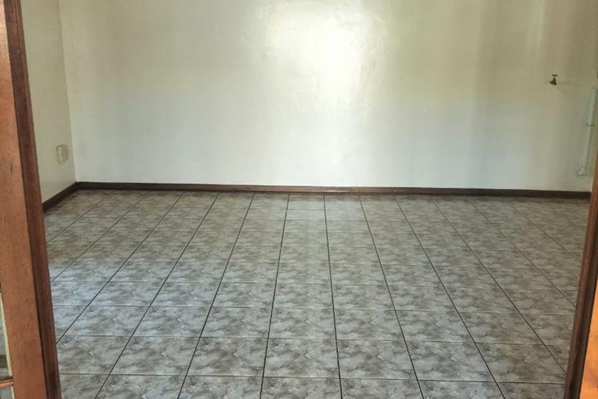An empty living room featuring ceramic floor tiles and a timber-paneled ceiling, providing a blank canvas for interior design.