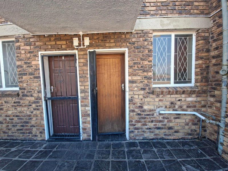 Rear exterior view of an apartment featuring face brick walls, a paved patio area, security gates, and timber door access.