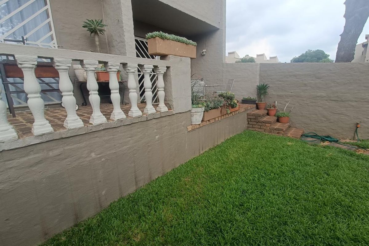 A private rear garden featuring a raised patio area with decorative balustrades, brick steps, and a well-maintained lawn.