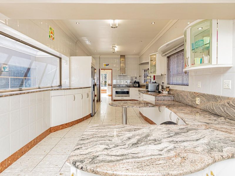Spacious kitchen featuring extensive granite countertops, white cabinetry, tiled flooring, and built-in cooking appliances, offering a functional layout with ample workspace.