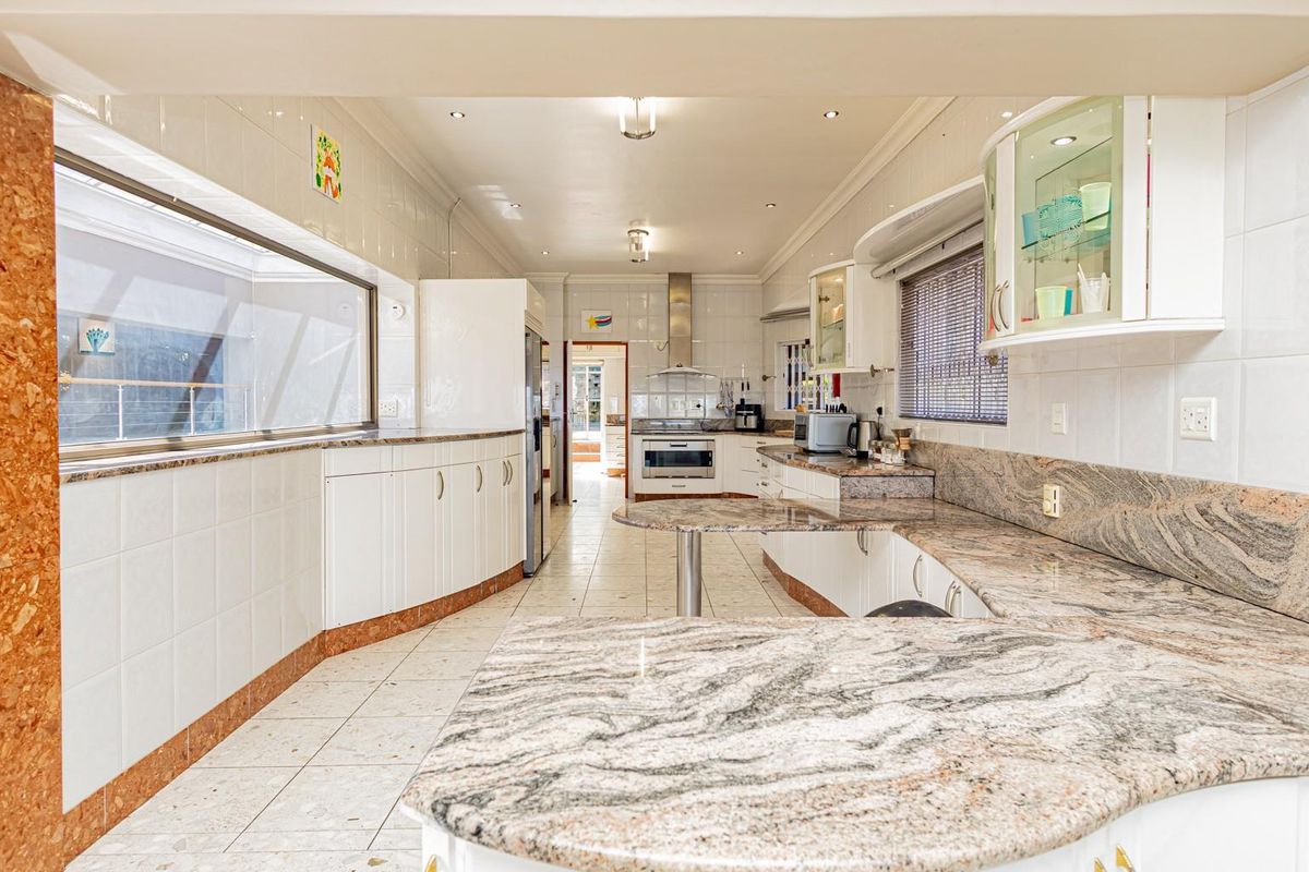Spacious kitchen featuring extensive granite countertops, white cabinetry, tiled flooring, and built-in cooking appliances, offering a functional layout with ample workspace.