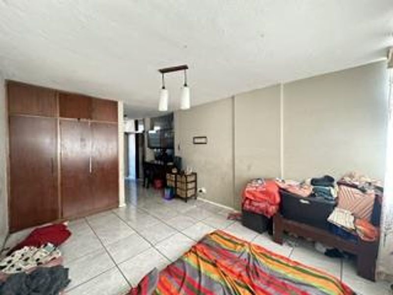 A bedroom featuring built-in wooden cupboards and tiled flooring, requiring cosmetic updates to the wall finishes.