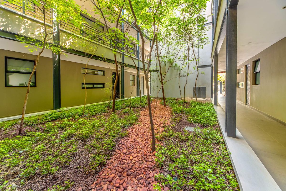 A well-maintained central courtyard featuring a pebble pathway, lush greenery, and covered walkways connecting the apartment building levels.