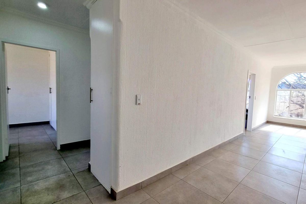 An empty, open-plan living area featuring neutral tiled flooring, textured walls, and a distinctive arched window allowing for natural light.
