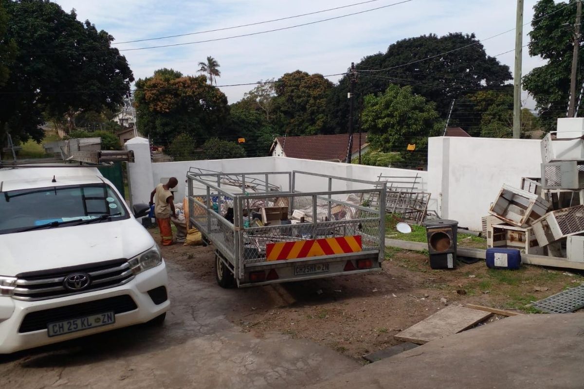 Rear exterior area of the property featuring a concrete driveway and perimeter wall, currently used for site maintenance and storage.