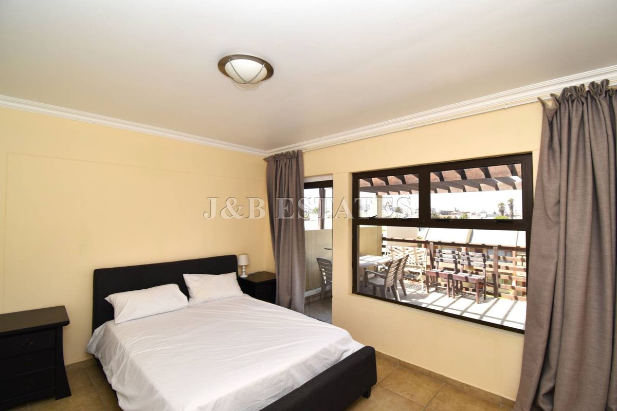 A bedroom featuring tiled flooring, crown molding, and a large window with direct access to an outdoor balcony area.