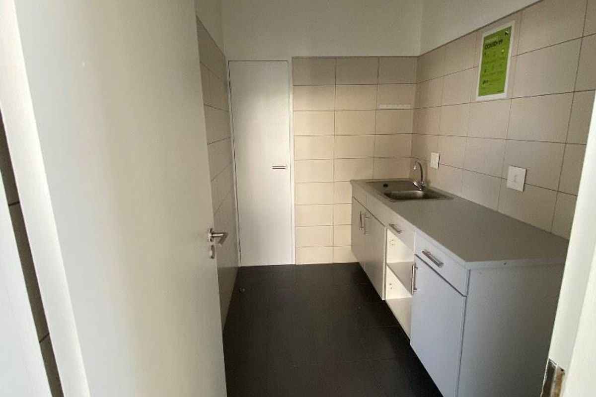 A functional office kitchenette featuring tiled walls, dark floor tiles, a built-in sink, and base cabinetry.