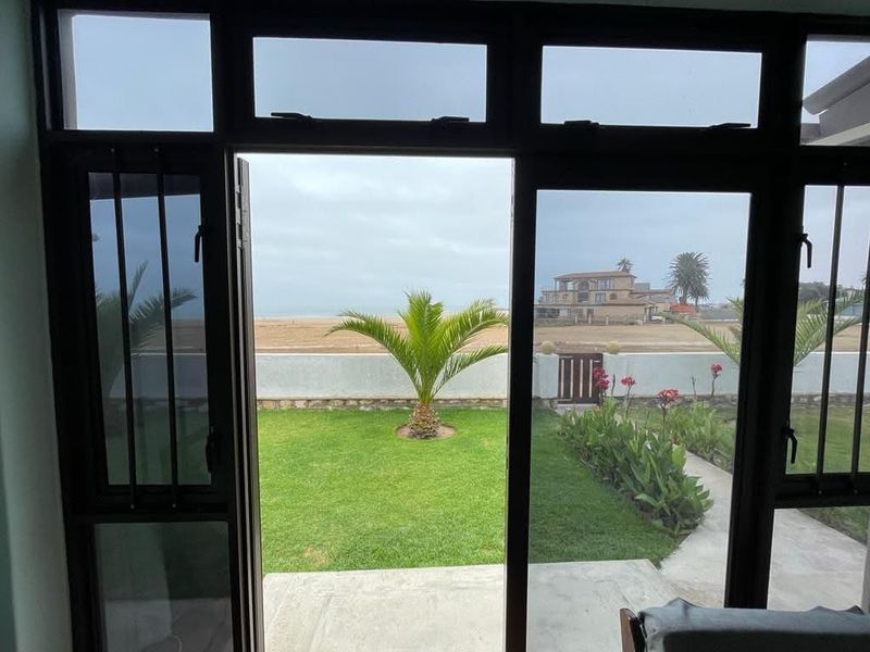 A view from an interior space looking out onto a private garden, boundary wall, and coastal landscape.