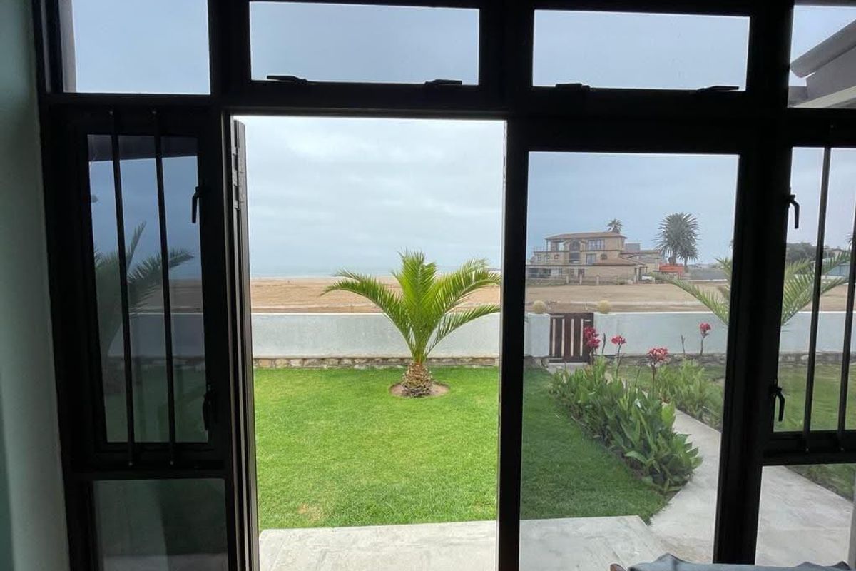 A view from an interior space looking out onto a private garden, boundary wall, and coastal landscape.