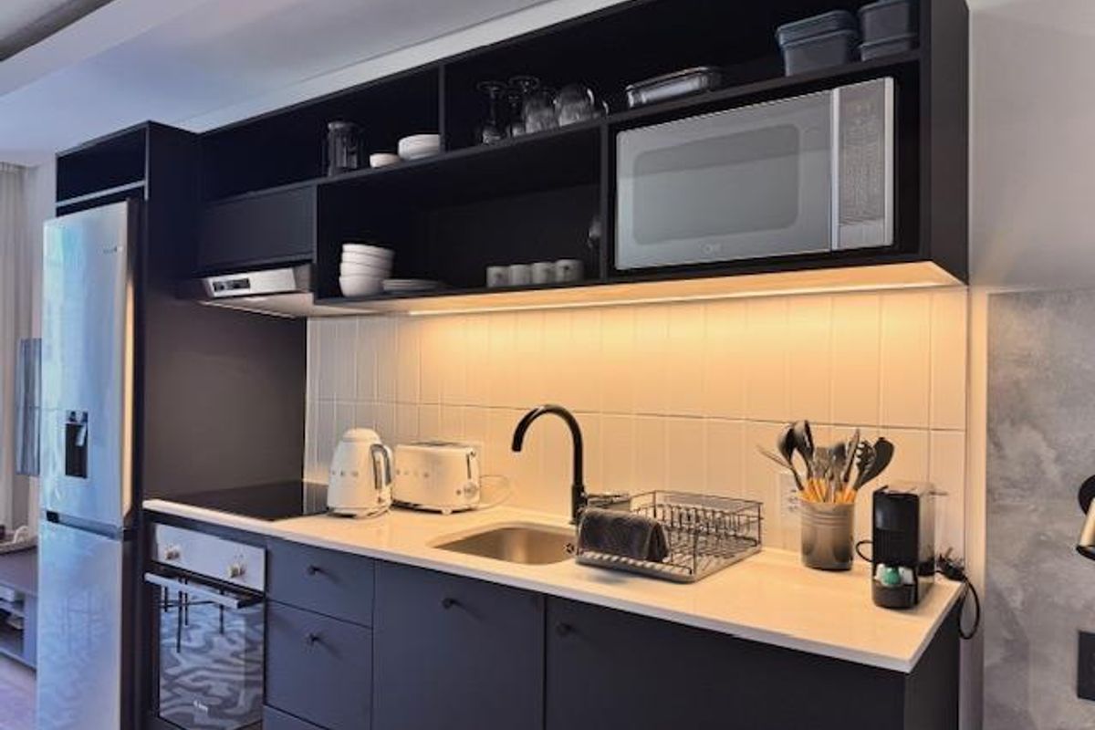 Modern compact kitchen featuring matte black cabinetry, integrated oven, induction hob, built-in microwave, and sleek subway tile backsplash with under-cabinet lighting.