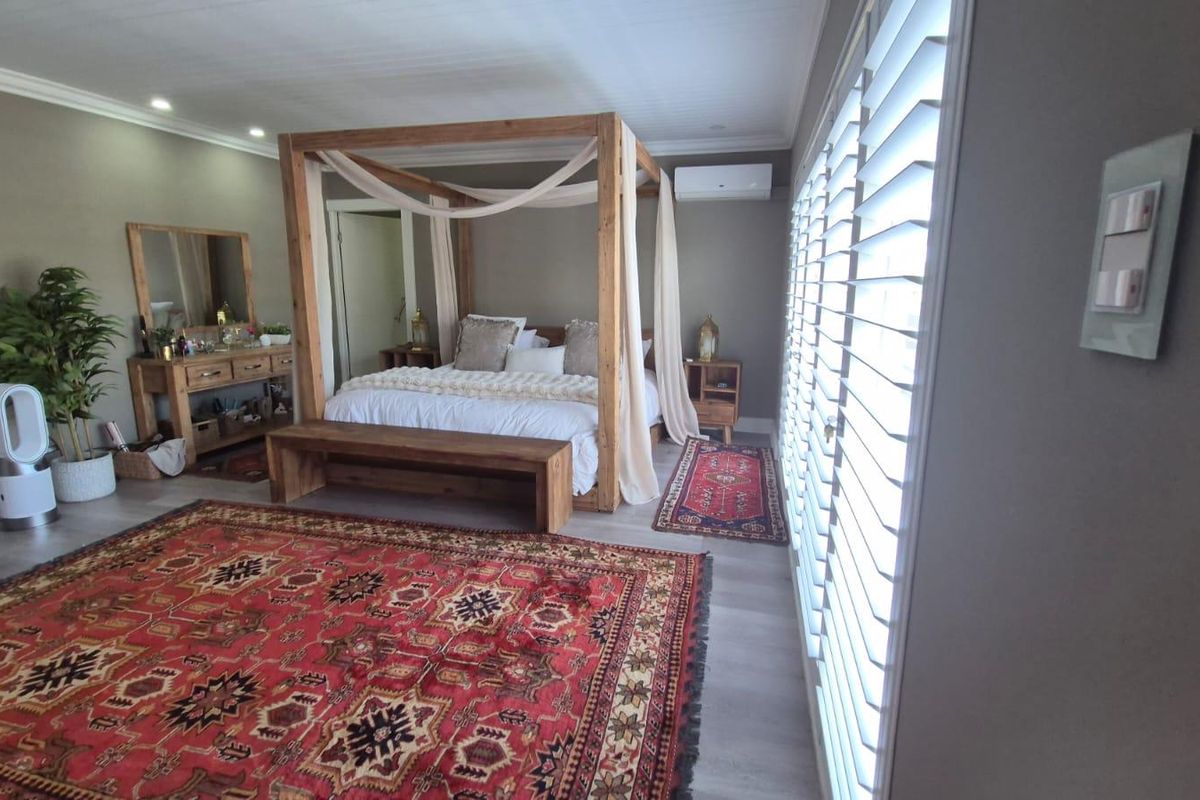Spacious bedroom featuring light-toned flooring, plantation shutters, and a wall-mounted air conditioning unit.